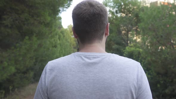 The back of a man dressed in basic gray T-shirt, who walks along a rural road surrounded by nature a