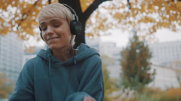 Close Up. Happy Young Woman in the Hoodie Dancing in the Park with Headphones in Autumn