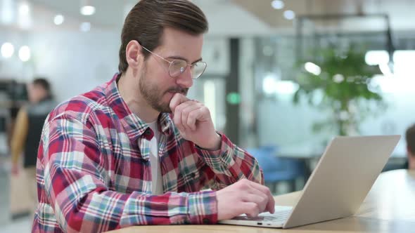 Pensive Male Designer Thinking and Working on Laptop