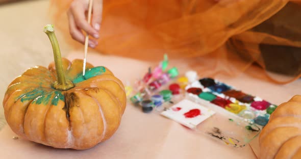 Little girl drawing face on orange Halloween pumpkin