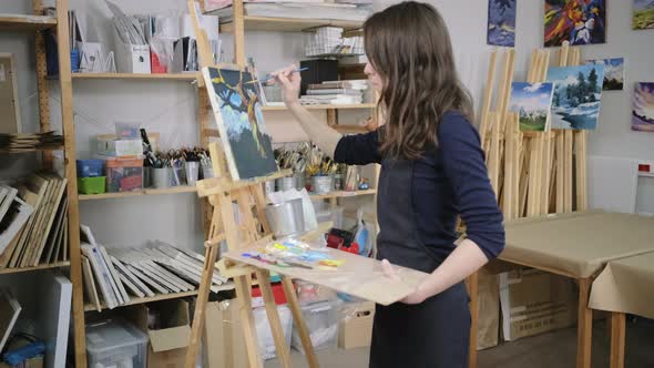 Student Artist Girl Is Holding Palette with Paints and Standing Near Easel