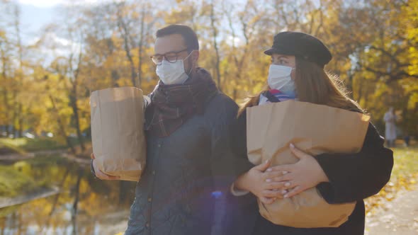 Portrait of Happy Couple in Safety Mask with Groceries Bags Walking in Fall Park