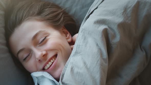 Young Woman with Long Hair Wakes Up, Gets Up on Bed and Stretches in Morning Sun Light