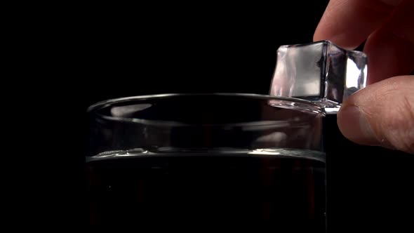 The hand of the bartender pushes an ice cube into a glass with alcohol or water 