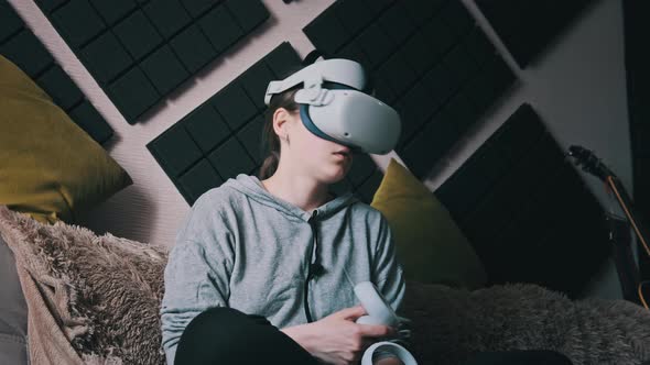 Young Woman in Virtual Reality Helmet Sitting on Sofa and Move Hands at Home