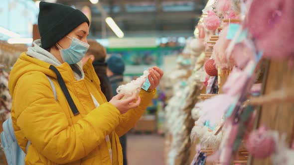 Woman in Yellow Winter Jacket Choosing Christmas Ornament on Christmas Market in Shopping Mall