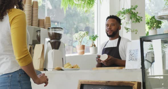 Happy african american male barista making coffee for biracial female client at cafe