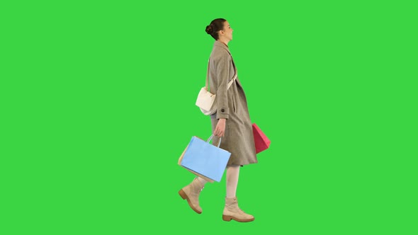 Young Woman in Stylish Clothes Walks Slowly with Colored Paper Bags on a Green Screen Chroma Key