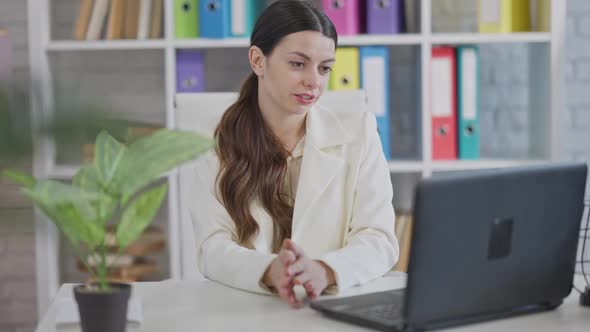 Positive Young Slim Woman Using Video Chat on Laptop Sitting in Office