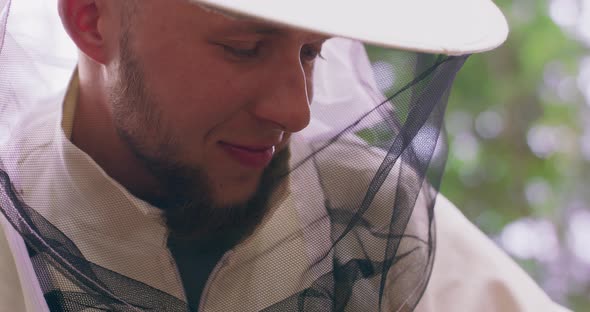 Closeup Face of Young Male Bearded Beekeeper in White Protective Suit Smiling Who Inspects the