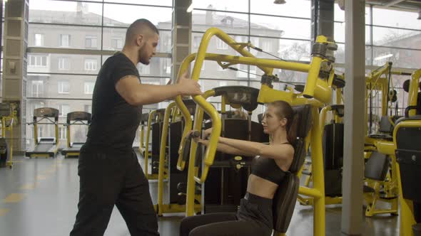 Young Woman with Instructor Using Chest Press Machine in Gym