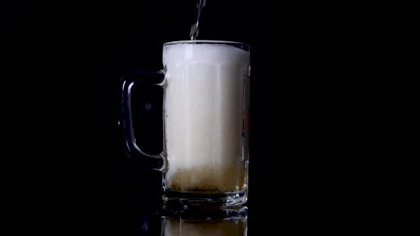 Slow motion shot of pouring beer in a mug until it spills over.