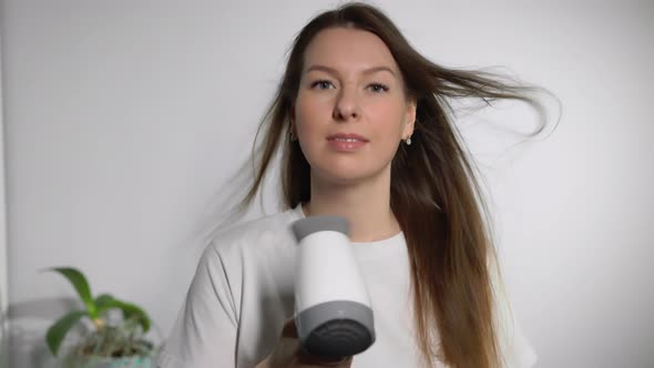 A Young Woman Dries Her Hair with an Electric Hair Dryer