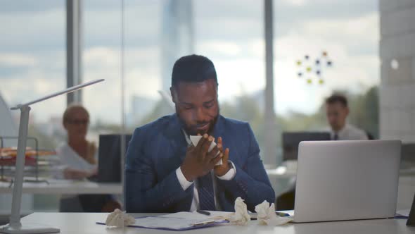 Sick African Manager with Sneezing in Tissue with Coworkers Working on Background in Office