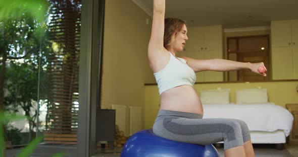 Caucasian pregnant woman exercising with weights and ball at home