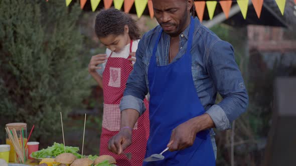 African American Focused Man Cleaning Spatula with Fork Standing on Picnic at Barbecue Grill