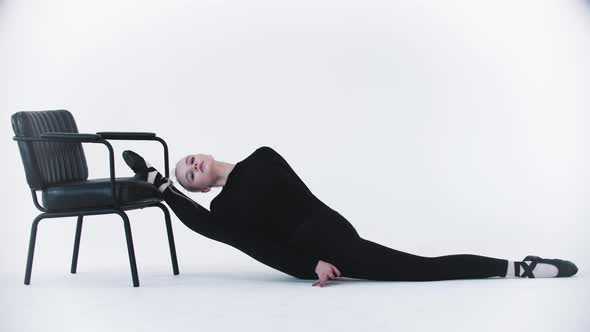 Young Blonde Woman Ballerina Putting on Her Leg on the Chair and Stretching