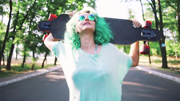 Portrait of Young Stylish Hipster Girl with Green Hair Walking with Long Board During Sunrise Slow