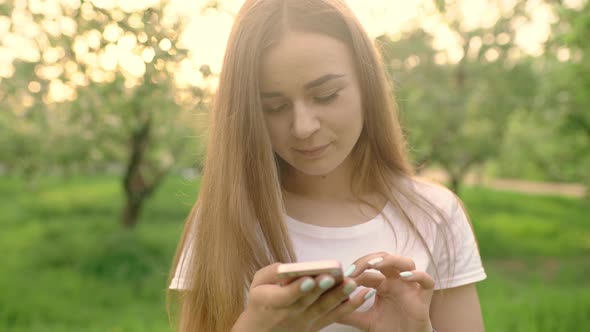 Portrait of a Beautiful Woman Typing on a Mobile Phone in the Park