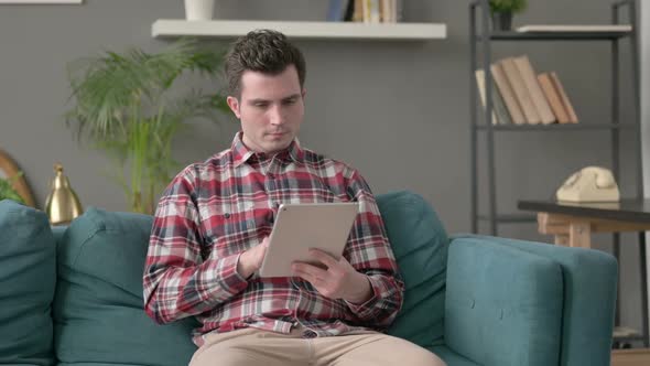 Man Celebrating Success on Tablet on Sofa