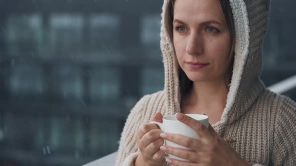 Woman Stays on Balcony During Snowfall with Cup of Hot Coffee or Tea