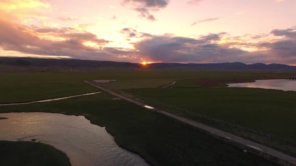 Aerial view flying backwards over winding river during colorful sunset