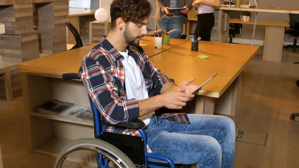 Male business executive sitting on wheelchair and using digital tablet