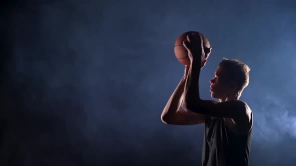 A Young Basketball Player in a Black Sports Uniform Makes a Jump Shot Side View