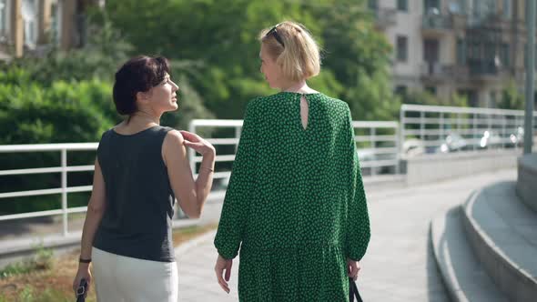 Back View Two Women Strolling on City Street in Slow Motion Talking Smiling