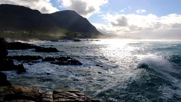 Wave reflecting beautiful morning light as it rolls past onto rocky coastline, with mountains in bac