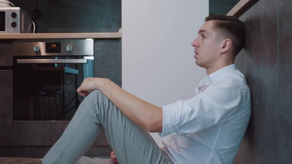 Heartbroken Young Man Sits on the Kitchen Floor and Cries