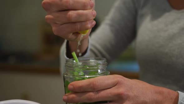 Caucasian woman squeezing lemon and preparing green vegetable smoothie in kitchen