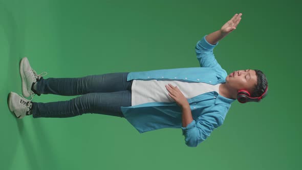 Full Body Of Asian Boy Listening To Music With Headphones And Dancing In The Green Screen Studio