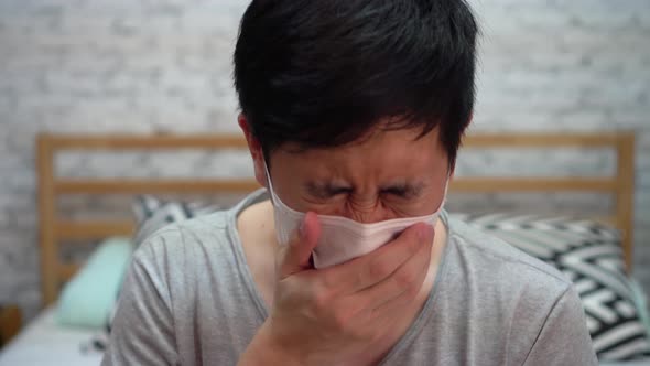 Young Asian Man Coughing and Suffering in Medical Mask Inside Home Bedroom