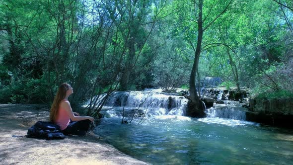 Woman is Sitting and Meditating in a Nature with a Waterfall