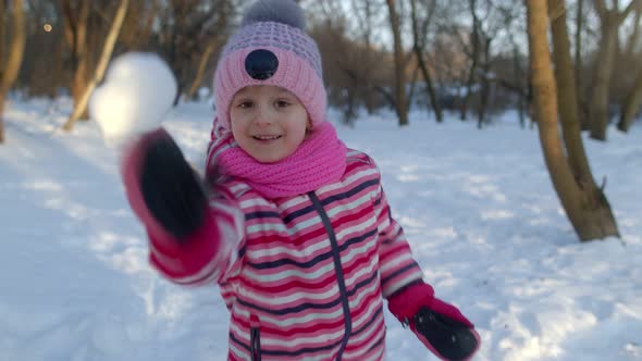 Cheerful Child Girl Throwing Snowball Snowflakes Into Camerafooling Around Smiling in Winter Park