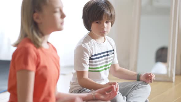 Portrait of Focused Caucasian Boy Sitting in Lotus Pose Looking at Blurred Girl at Front