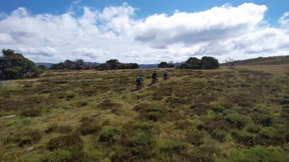 Drone following behind mountain bike riders anding up alongside them on the top of a mountain trail.