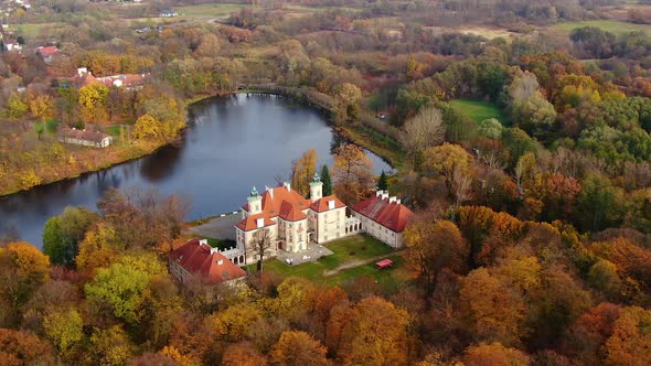 Palace by a lake or castle in forest. Autumn colorful woods and big impressive fairy tale building.