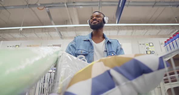 AfricanAmerican Man Customer in Headphones Walking with Cart in Houseware Store