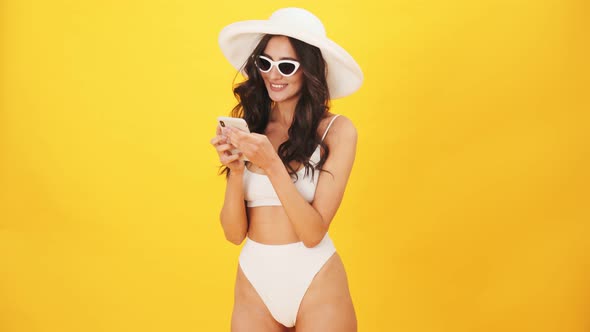 A pleased brunette woman wearing a swimsuit using her mobile