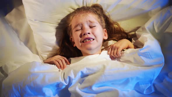 A sweet little girl naps in bed in her room, sees a nightmare and fears in her sleep