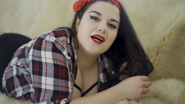 Pretty Plus Size Girl with Bright Make-up Lying on the Sofa Posing Looking in Camera