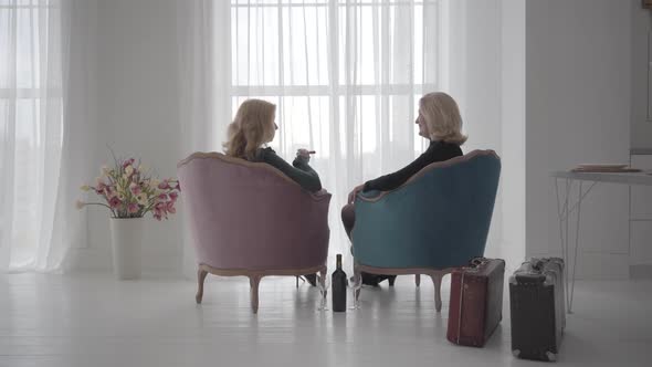 Back View of Rich Mature Caucasian Women Sitting in Comfortable Armchairs and Talking