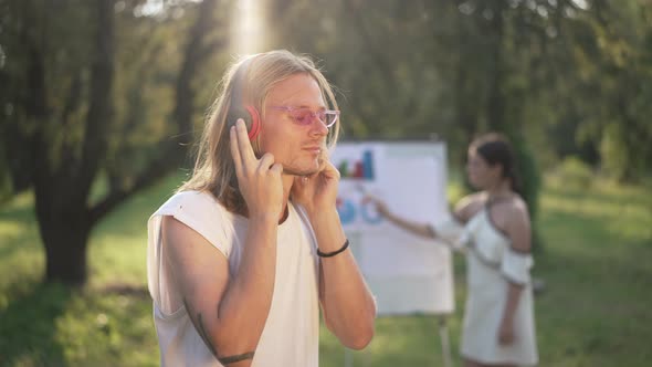 Positive Caucasian Man Listening to Music in Headphones Smiling Standing in Sunrays on the Left with