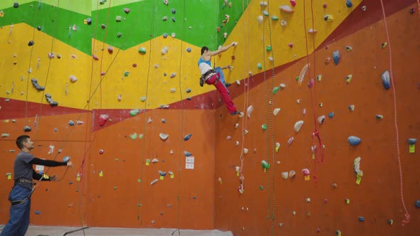 Rock climbers indoor, Belayer watching leading climber