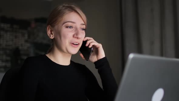 Happy Young Woman Talking and Laughing on Phone and Using Laptop Sitting at Home