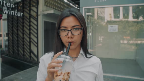 Portrait Shot of an Asian Attractive Young Woman Wearing Glasses Drinking Cold Coffee Outside