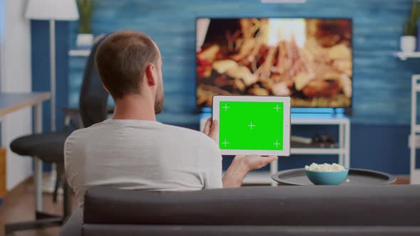 Back View of Man Holding Digital Tablet with Green Screen Watching Social Media Video Content