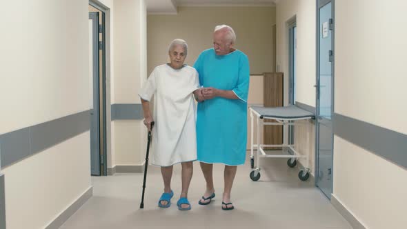 Old man helping old woman with stick to go through hospital